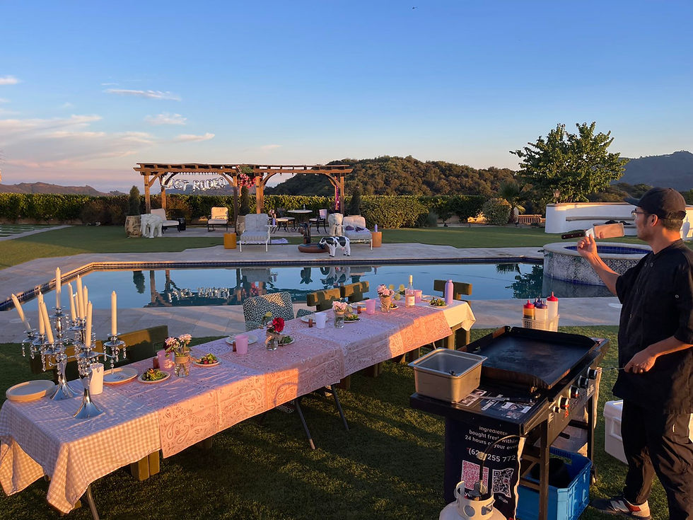 A chef flips a knife near a table set with candles and flowers by a pool. "Just Married" sign in the background. Calm, evening ambiance.