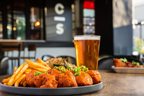 A plate of buffalo wings and french fries on a table with a pint of beer