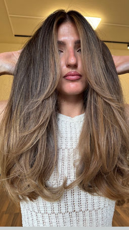 Front view of a woman with a luxury caramel balayage featuring a seamless root melt, soft face-framing highlights and long, glossy hair styled in soft waves at Emberyl Hair Atelier in Zürich.