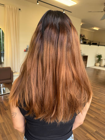 Front and back view of a colour correction from warm copper hair to a seamless blonde balayage with a soft root melt, face-framing highlights and glossy waves at Emberyl Hair Atelier in Zürich.