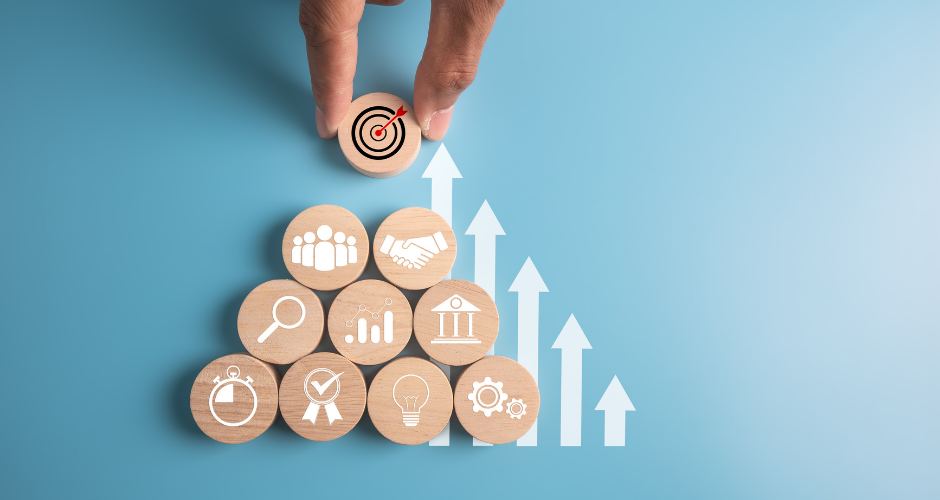 Hand placing a target icon atop stacked business symbols with upward arrows, illustrating how to align marketing strategy with business objectives.