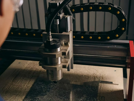 A person operates a CNC machine in a workshop setting. The machine engraves metal under a spotlight. The mood is focused and industrious.