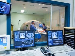 Two medical staff operate a preventive screening in a control room, surrounded by monitors showing scans. The setting is clinical and efficient.