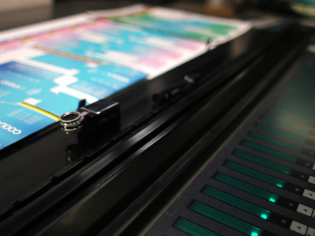 Close-up of a printing press with vibrant multicolored prints, adjustable dials, and glowing controls in a production setting.