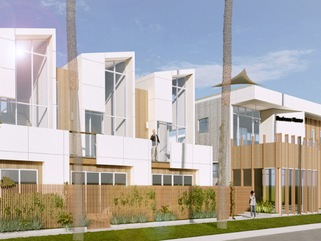 Modern building with white and wood accents, featuring large windows and greenery. Two people stand on a balcony, palm trees in view.