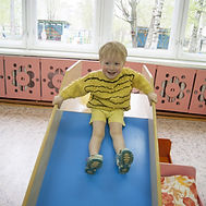 Occupational Therapy: A young child sitting at the top of a small indoor slide.
