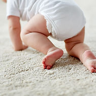 Close-up of a baby's legs and feet as they crawl on a grey carpet.