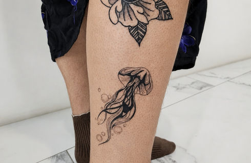 Blackwork jellyfish and flower tattoos with fine line details on the lower leg.