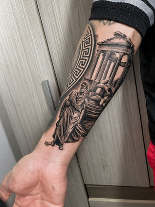 Black and grey realism forearm tattoo featuring a Greek philosopher statue, ancient temple ruins, and classical architecture at White Sloth Tattoo Shop in Tamarindo, Costa Rica.