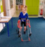 An 8-year-old girl with a walker and a belt cane walks down the school hallway with a smile on her face