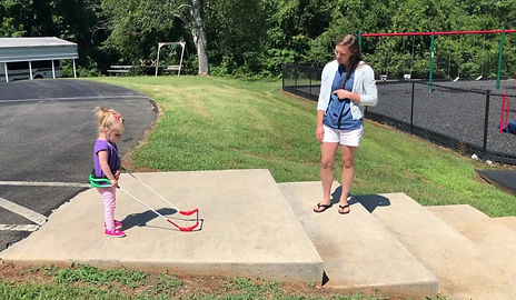 Madison is walking down steps wearing her belt cane holding her mom's hands