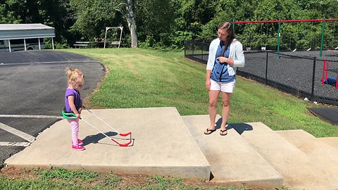 Madison is walking down steps wearing her belt cane holding her mom's hands