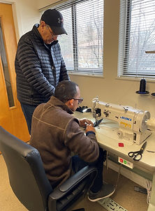 two men, one standing, one sitting by industrial sewing machine