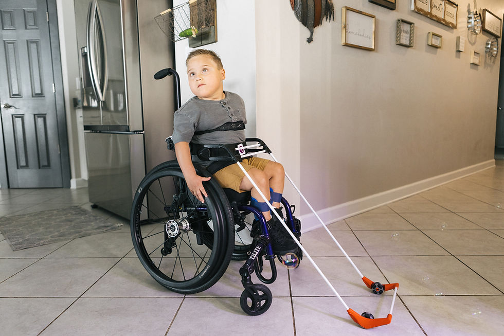 Eye-level view of a boy in a wheelchair wearing a belt cane in his family's kitchen.
