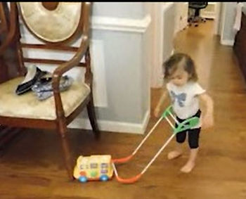 Charn stands with the base of the belt cane in contact with a wheeled, musical school bus toy.