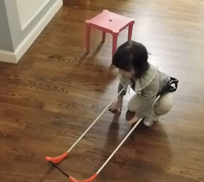 a blind 2-year-old wearing a belt cane stands up from the floor