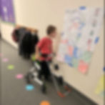 in school hallway a boy wearing a belt cane and using a walker views a poster on the wall more closely.