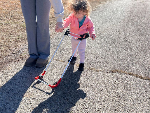 a 2-year-old girl with CVI wearing a Belt Cane outside holds an adult's hand while walking