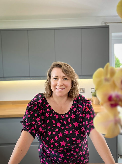 Gemma Hall, Heartbreak and Trauma Recovery Coach stands in a grey kitchen wearing a Scamp & Dude dress