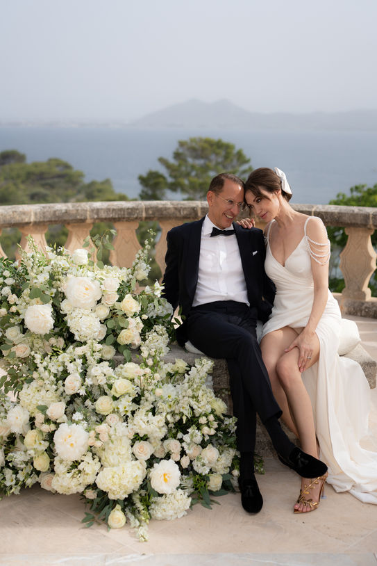 Bride and groom sitting on floral arrangement at Mallorca wedding