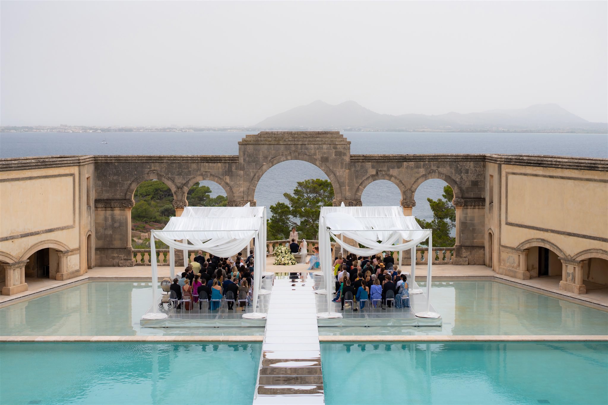 Outdoor wedding ceremony setup by a pool with stone arches and water reflections in La Fortaleza
