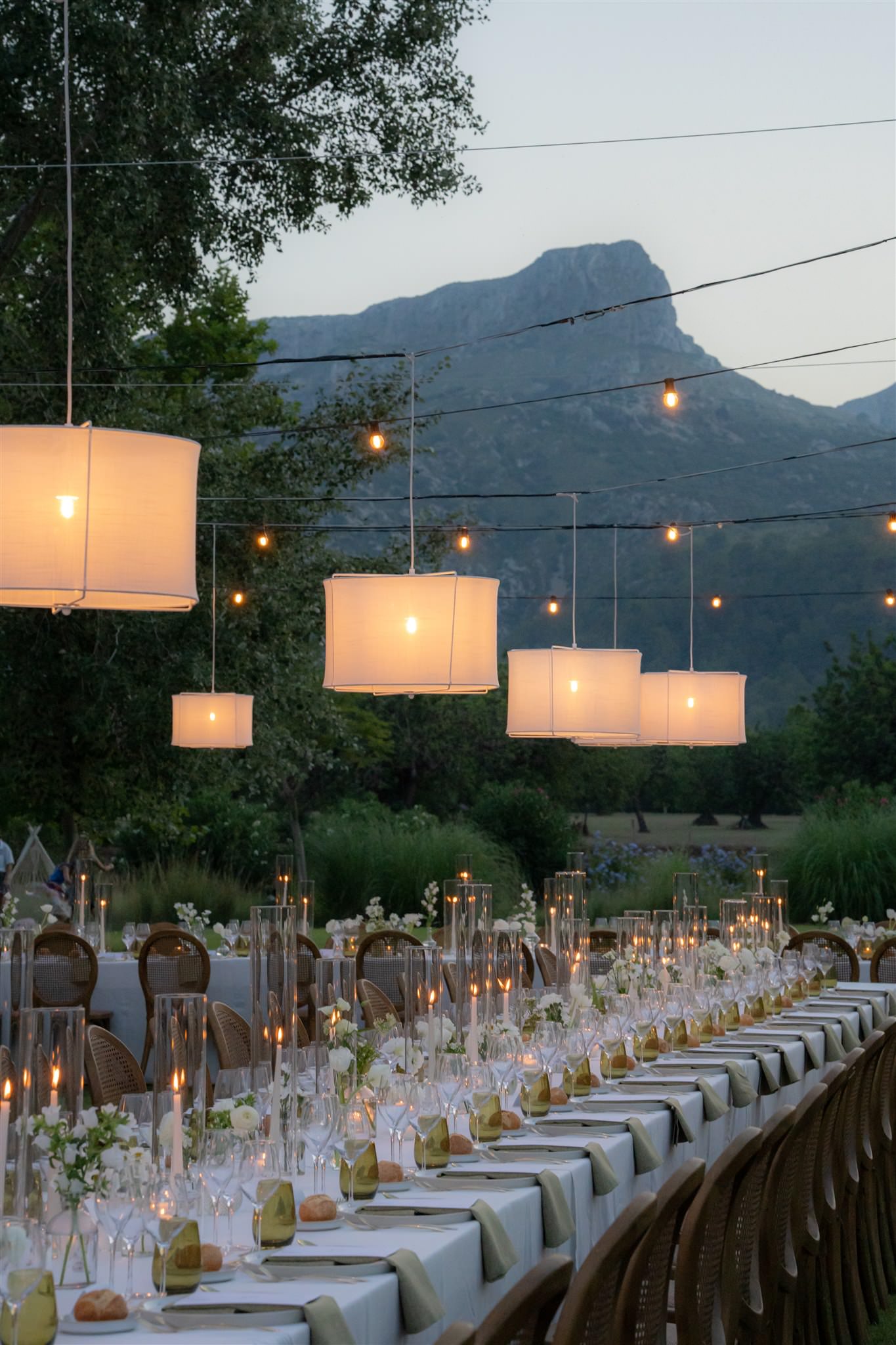 Long dinner table setup with candles and hanging lights at an outdoor wedding dinner in Almond Valley