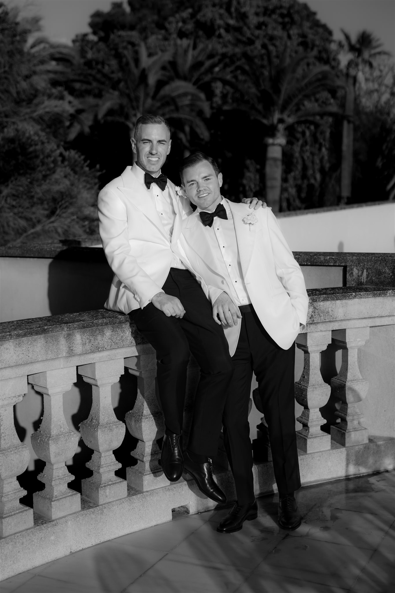 Black and white image of two grooms standing on balcony in formal attire during wedding day at Son Julia Country House