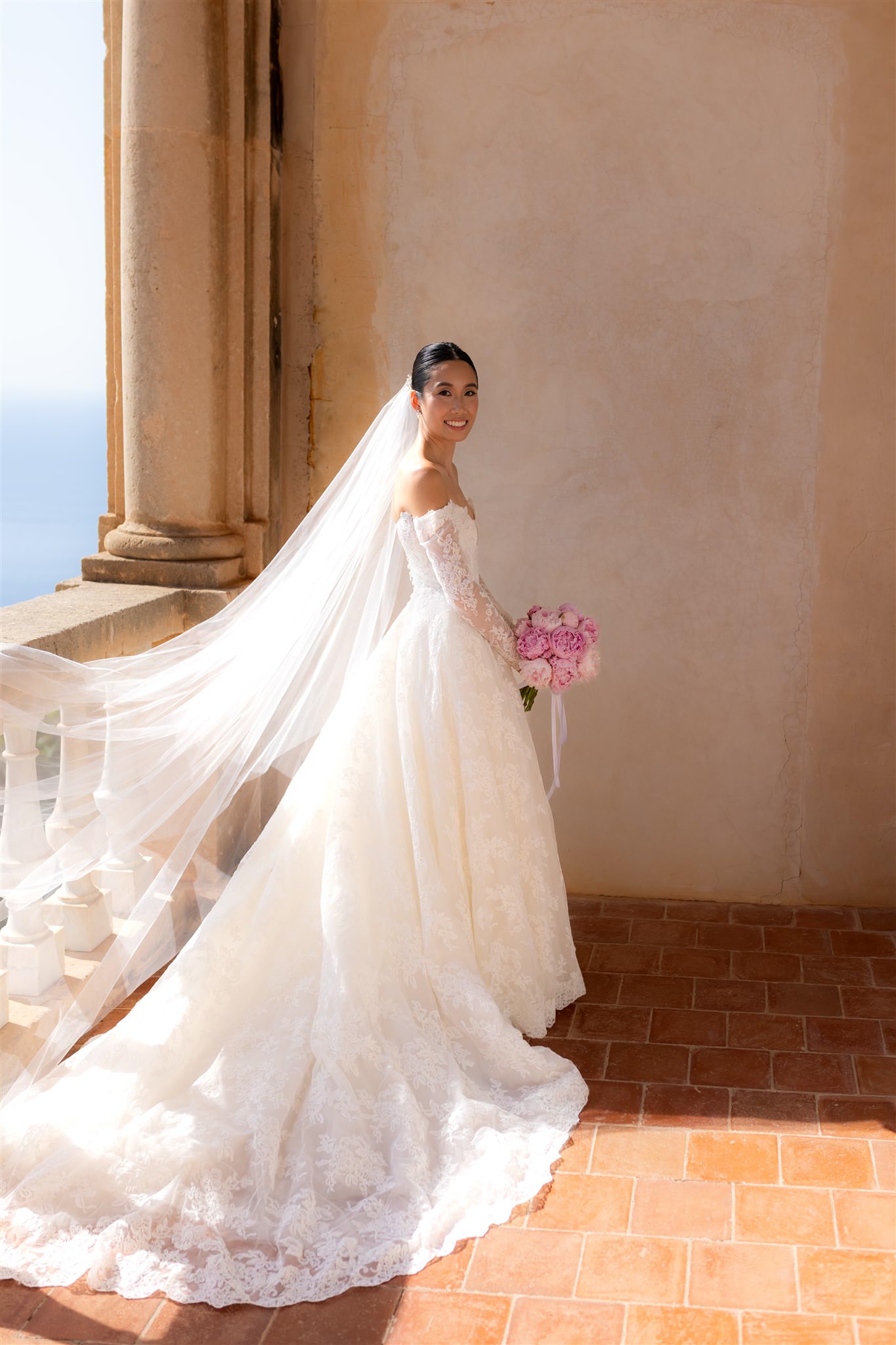bride standing in a wedding dress with long veil and soft natural light on the balcony in Son Marroig