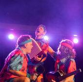 Drei Künstler in bunten Kostümen tanzen und musizieren auf der Bühne Bühnenpolka.