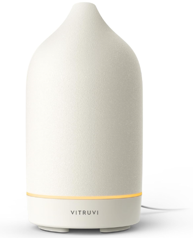 White Vitruvi diffuser emits a soft glow, set against a plain background. Its minimalist design and subtle light create a calm mood.