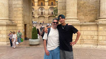 Dos personas posan abrazadas ante una puerta monumental de piedra en Córdoba.