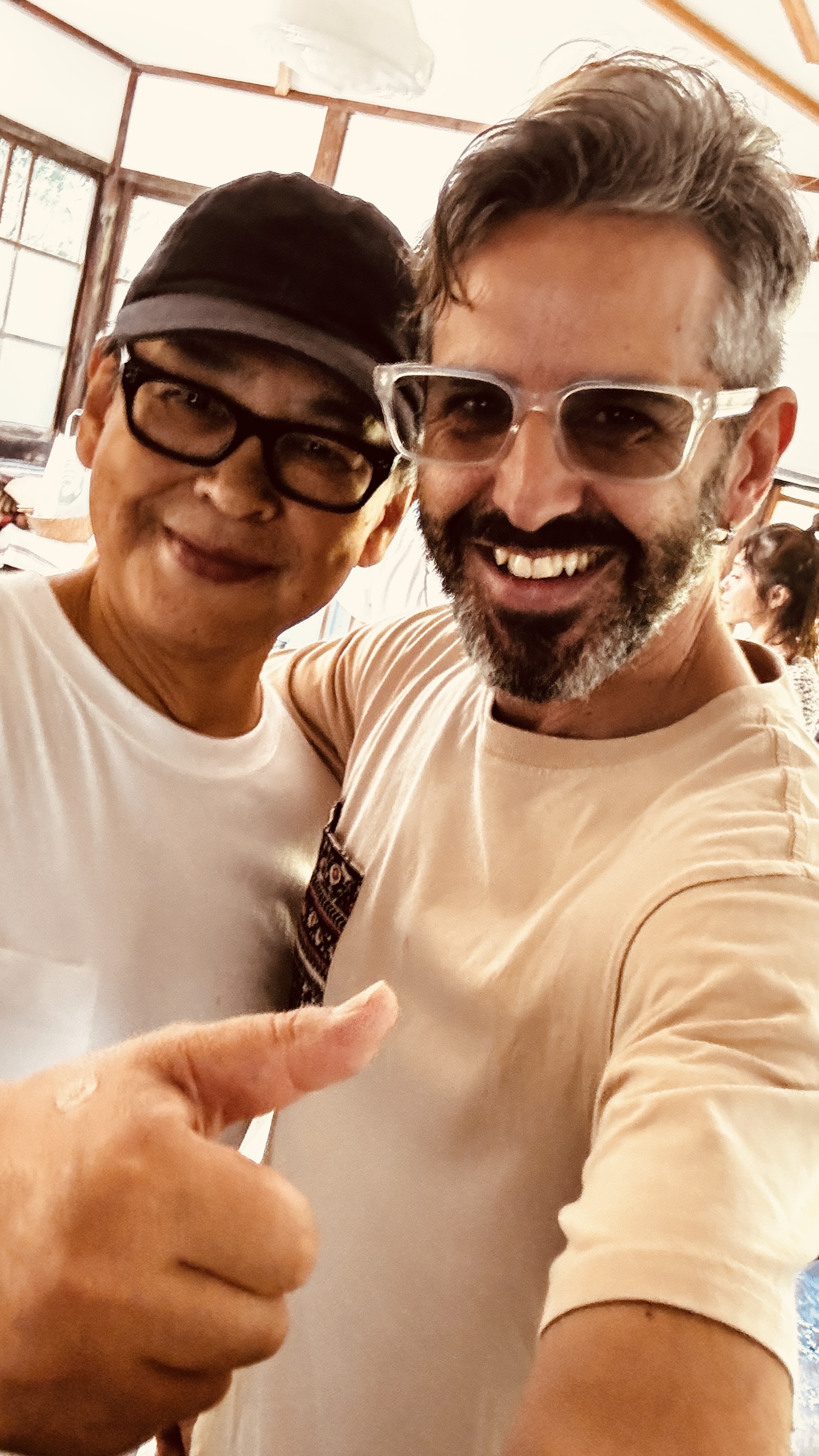 Un selfi en primer plano de dos personas en un interior; una lleva una gorra oscura.