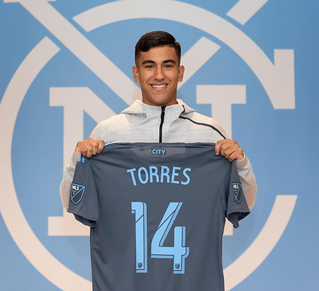 Coach Juan Pablo proudly holding his jersey from his professional soccer career, symbolizing his experience with NYCFC. 