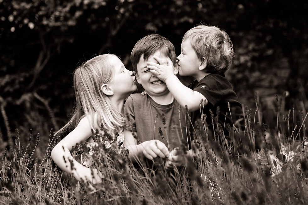 Two boys and a girl in a garden. The girl and young boy are kissing the middle boy
