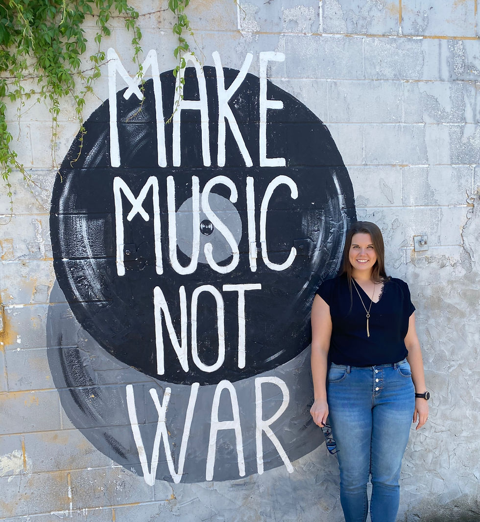 Picture of me next to a mural that reads "Make music not war"