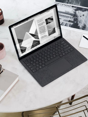 A desk with laptop, glasses resting on a book, and a drink with a dessert