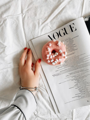 A donut with pink icing and some little white marshmallows sprinkled on it, and it is sitting on an open magazine page