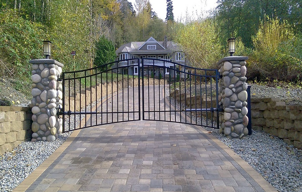 an ornamental metal automated double swing gate with rock wall pillars on either side
