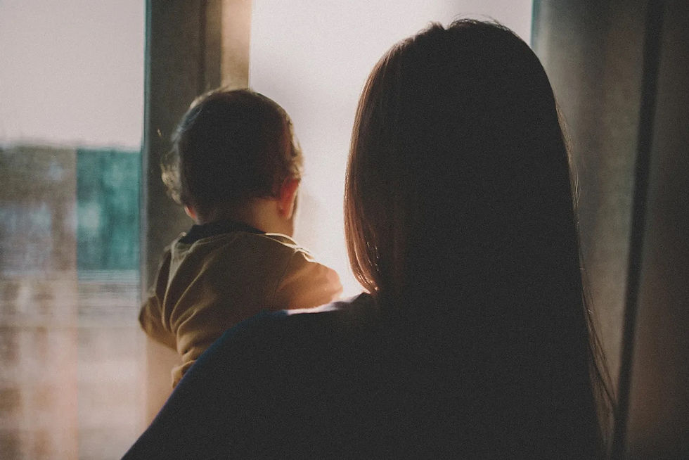 woman holds baby while looking out a window.