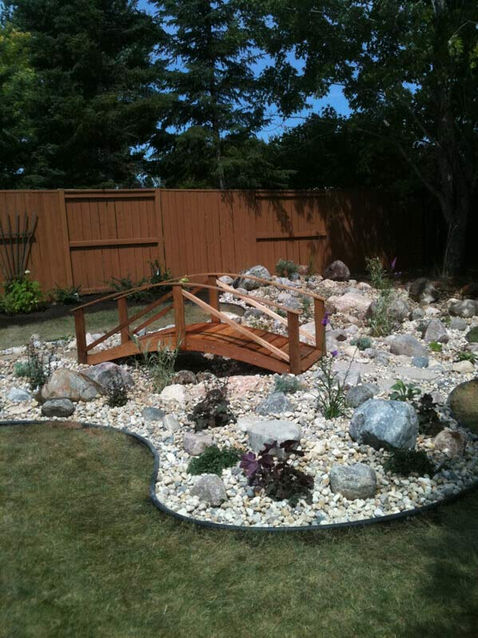 Wooden bridge over decorative stone and rocks in landscaped backyard setting.