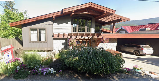 Modern house with wooden beams, landscaped yard, and car in carport. For sale.
