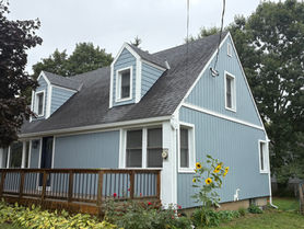 Blue cape house with dormers, wooden deck and sunflowers