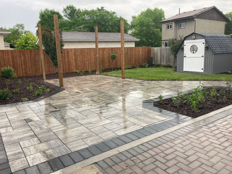 Grey paved patio with wooden posts and green lawn in residential backyard.