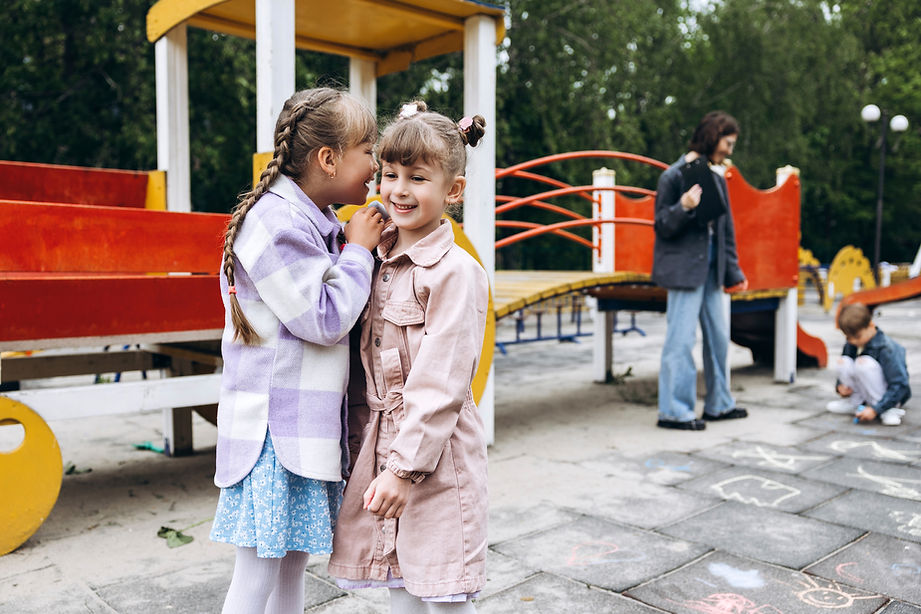 Two young girls whispering and laughing at a playground.