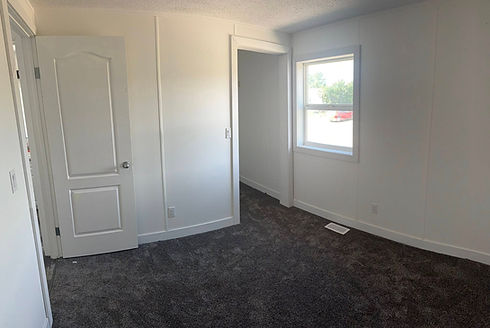 Empty room with white walls, dark gray carpet, white door, and window.