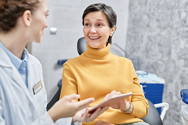 Portrait of smiling mature woman in dental clinic talking to female dentist and holding ta