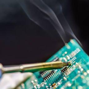 Soldering iron on a circuit board with smoke, close-up shot.