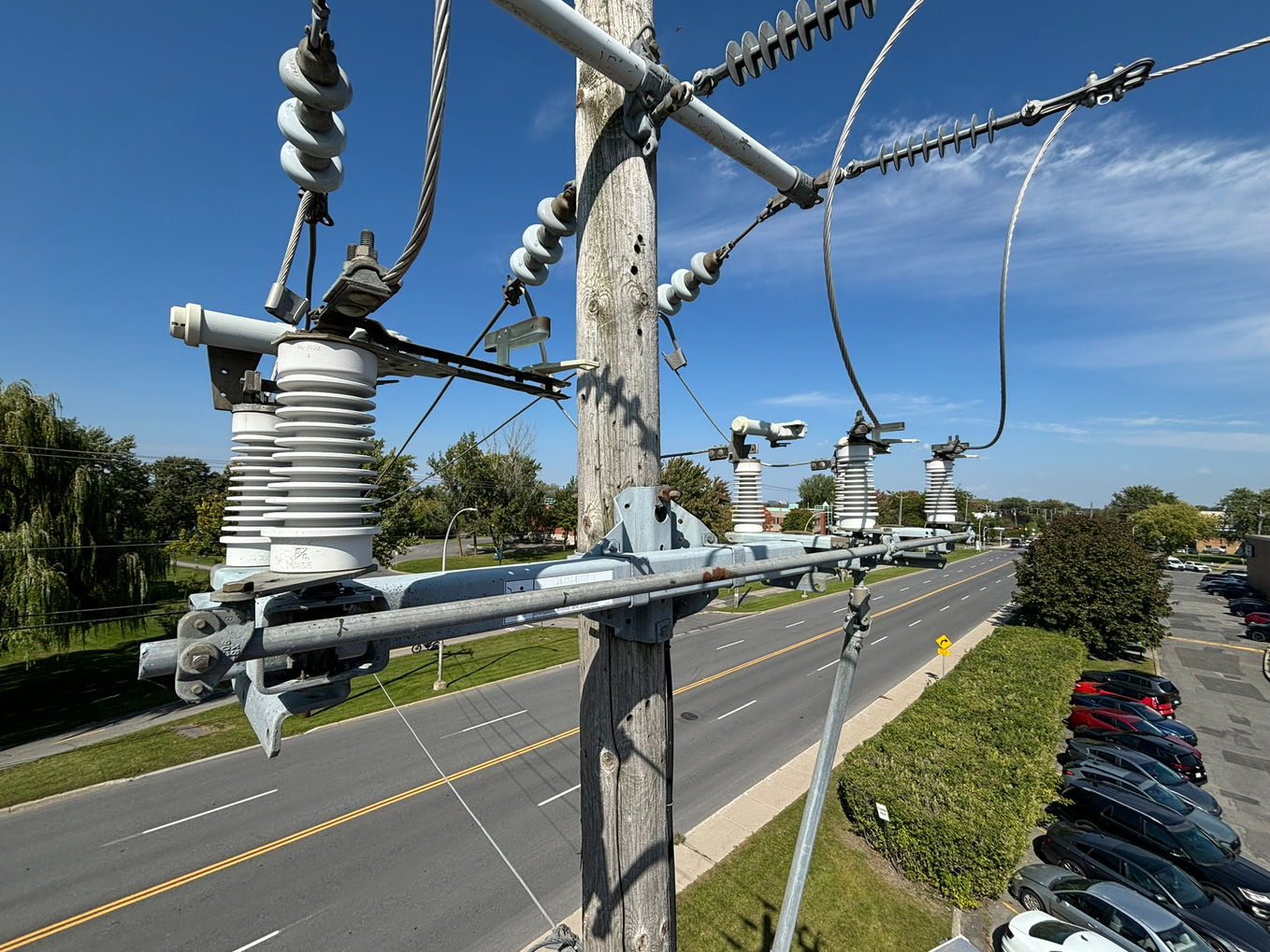 Electric pole with wires, transformers above a busy road, blue sky.
