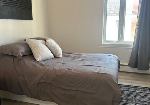 Chambre d'un appartement meublé avec lit double et fenêtre.