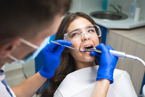dentist in mask filling the patient's root canal while she is lying on dental chair in saf